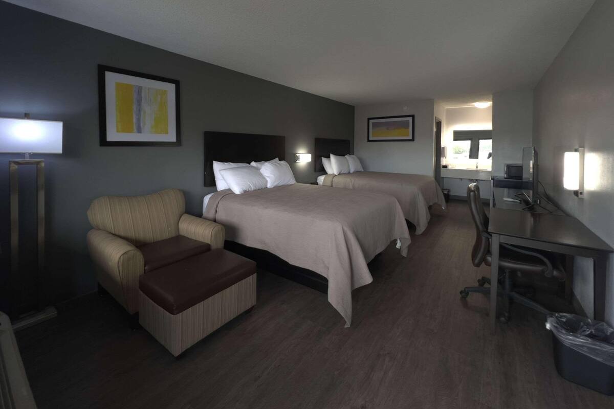 Une chambre d’hôtel avec deux lits, un bureau, une chaise, une lampe et une poubelle.