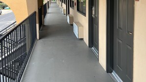 Corredor com portas de um lado e corrimão do outro, dando acesso a quartos individuais.