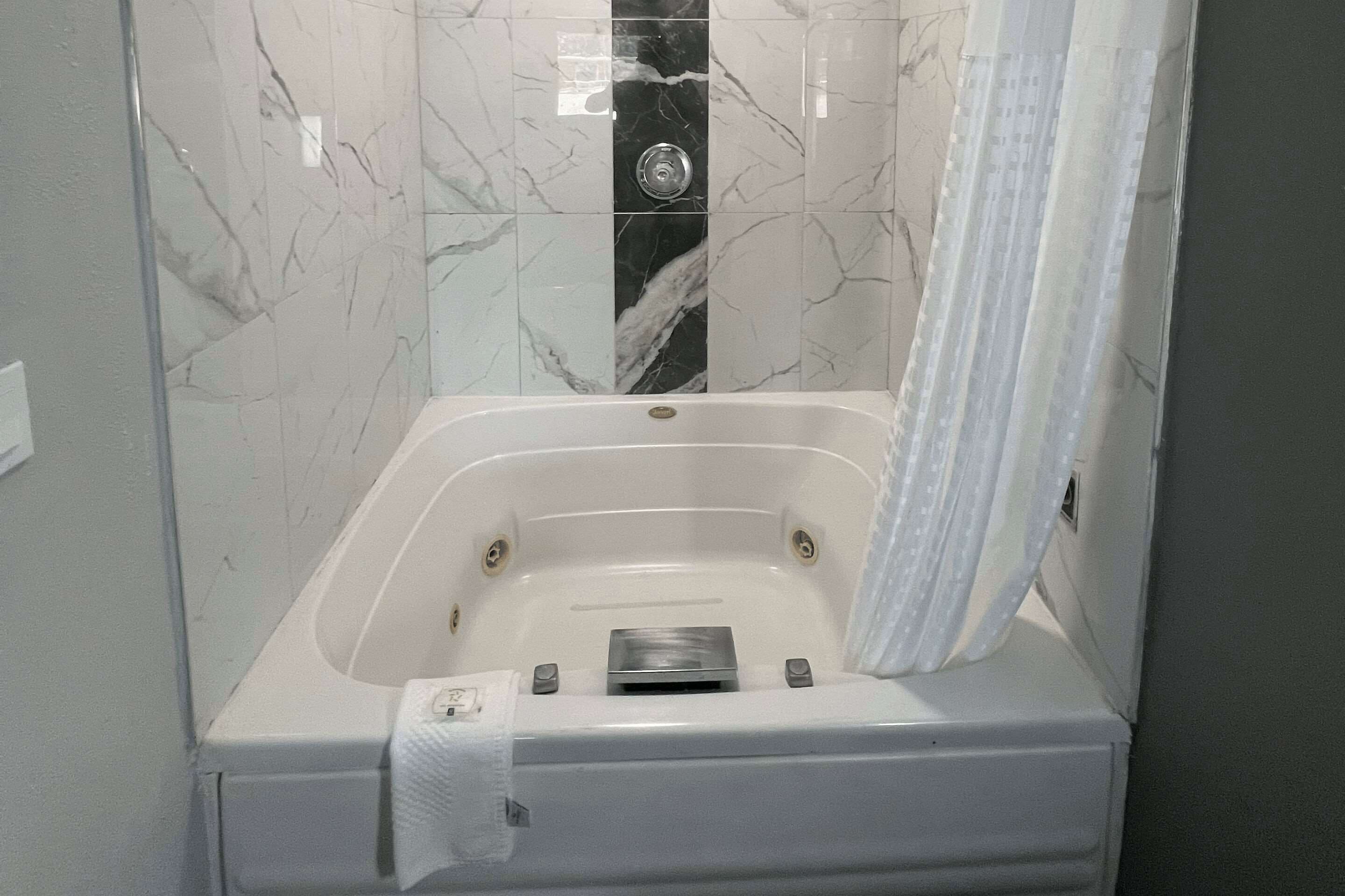 Une salle de bain moderne avec une douche à l’italienne aux carreaux de marbre, une baignoire blanche et un distributeur de serviettes.
