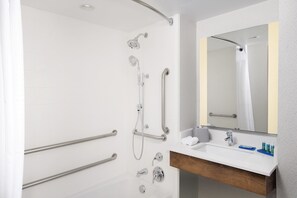 A modern bathroom with a walk-in shower, grab bars, a sink with a mirror, and toiletries. - Holiday Inn Express & Suites College Park-University Area by IHG (College Park)