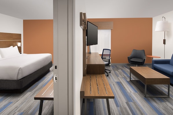 Quarto de hotel com cama, escrivaninha, cadeira, televisão e luminária.