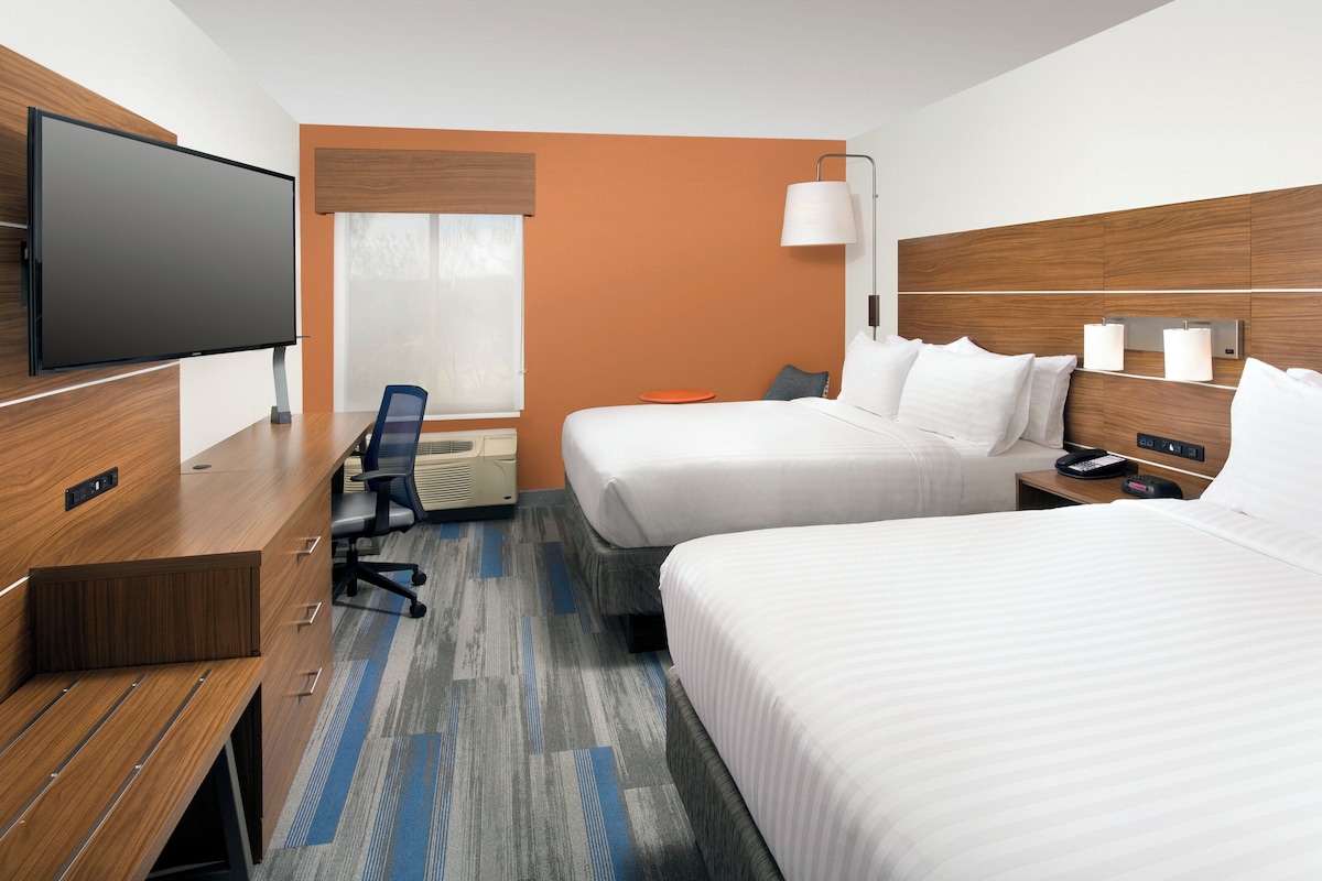 Quarto de hotel com televisão de tela plana, duas camas, escrivaninha e uma cadeira.