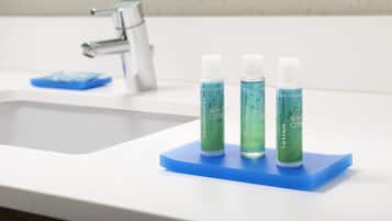 A bathroom sink with three bottles of white lotion and a blue soap dish.