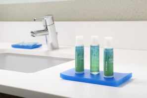 Uma pia de banheiro com três frascos de loção branca e um saboneteiro azul.
