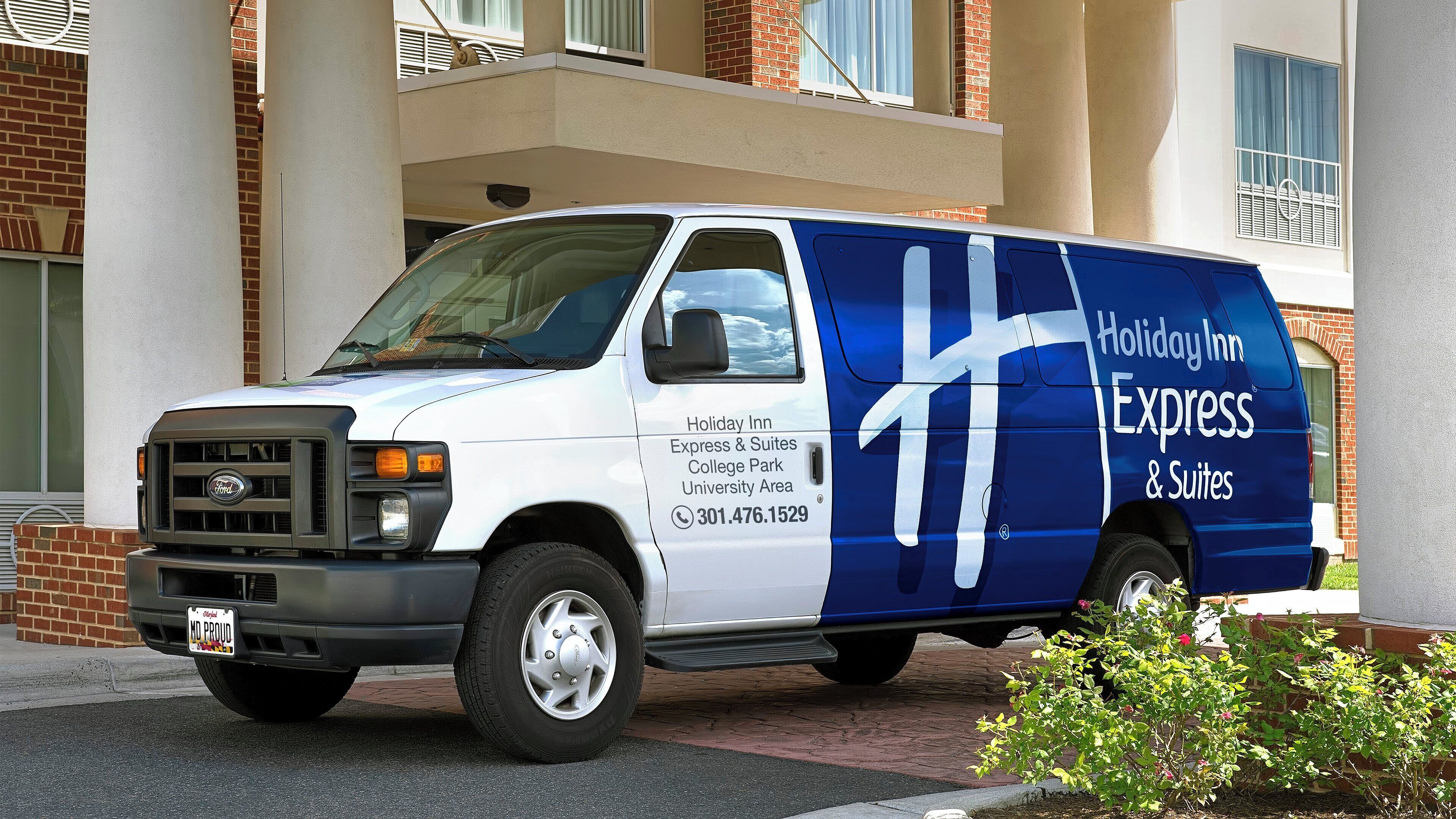 A white and blue van with 'Holiday Inn Express & Suites' branding parked in front of a building with a brick facade.