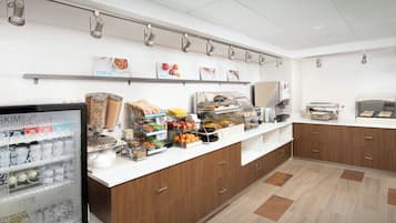 Zona de desayuno tipo buffet con diferentes opciones de comida y una vitrina refrigerada con productos lácteos.