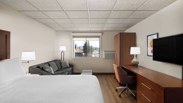 A hotel room with a bed, a desk, a chair, a television, and a window with a view of trees and mountains.