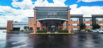 Un edificio comercial con un llamativo letrero 'Garnier BY IHG', un acceso cubierto y un estacionamiento.