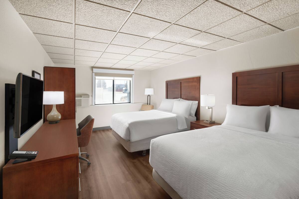 A hotel room with a large bed, a smaller bed, a desk with a computer, a TV, and a window with a view.