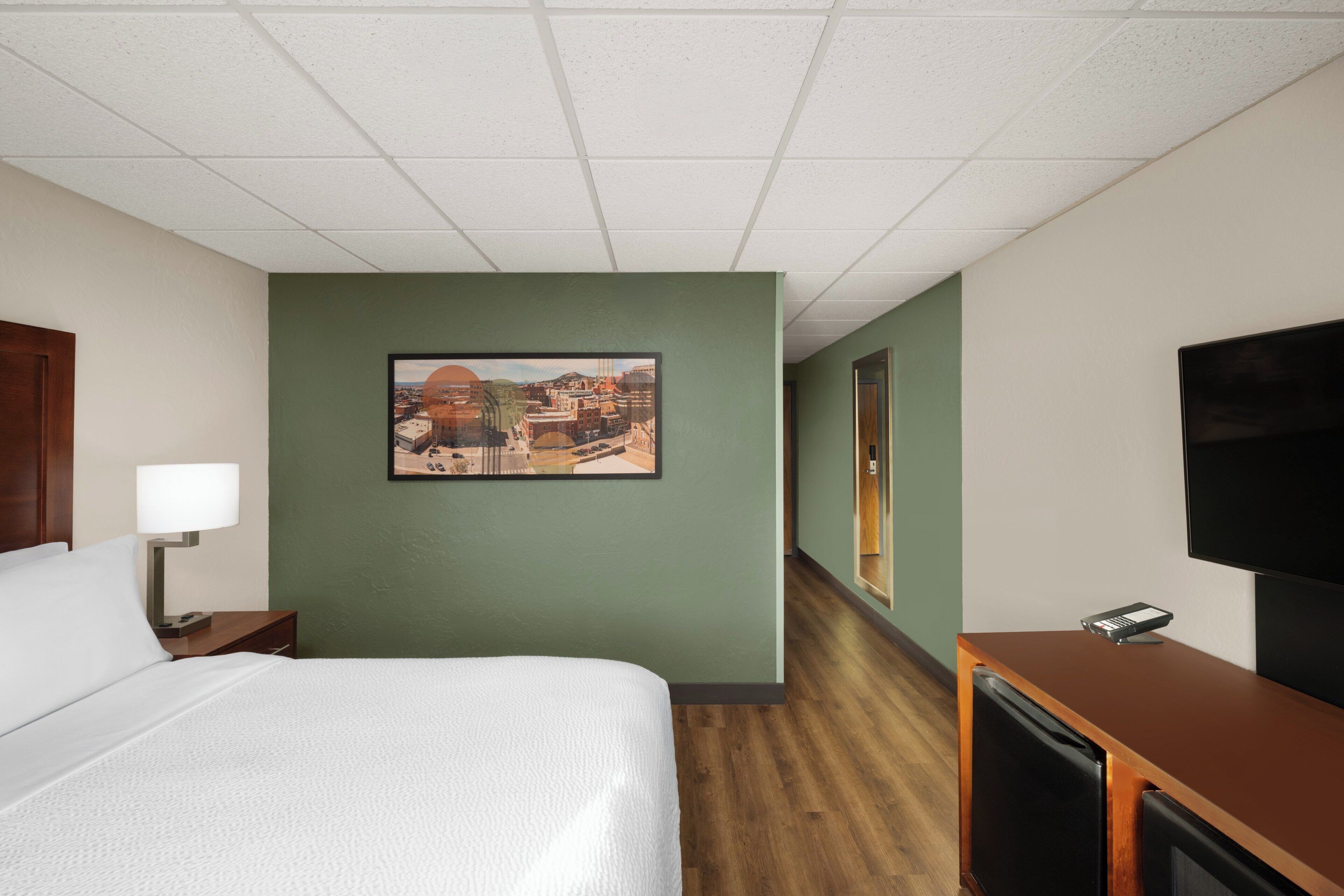 Habitación de hotel con cama, escritorio, televisión, un cuadro en la pared y ventana.