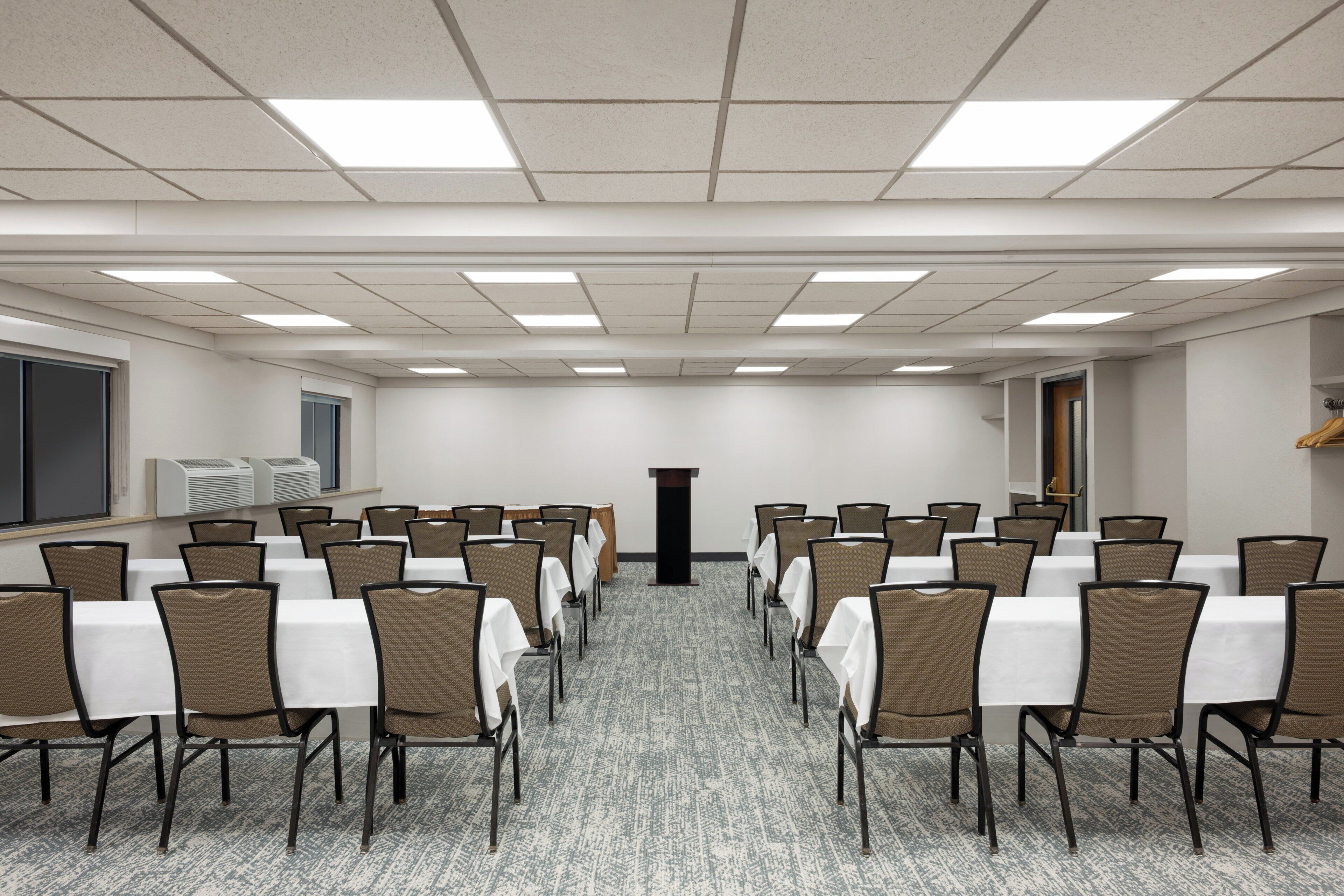 A conference room with rows of tables and chairs, a podium, and a carpeted floor.