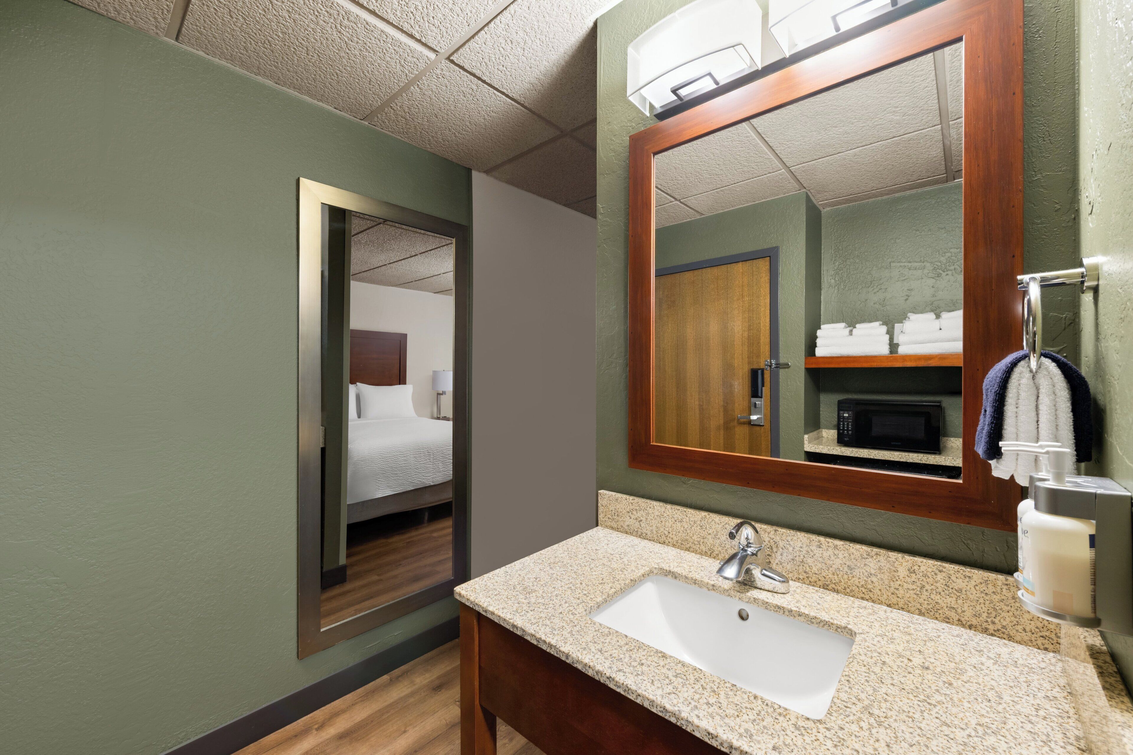 A hotel bathroom with a sink, mirror, and a door leading to a bedroom.