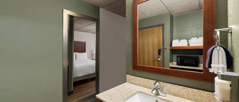 A hotel bathroom with a sink, mirror, and a door leading to a bedroom.