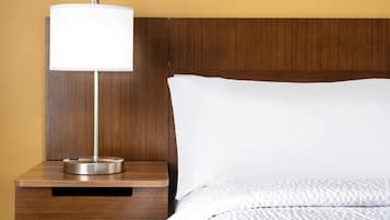 A neatly made bed with a white pillow and a wooden nightstand with a lamp.