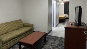A hotel room with a green-striped sofa, a wooden coffee table, a television on a stand, and a patterned rug. - Baymont by Wyndham Omaha SW (Omaha)