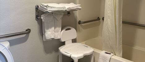A small bathroom with a toilet, a white pedestal sink, a shower with a beige curtain, and a towel rack with folded towels.