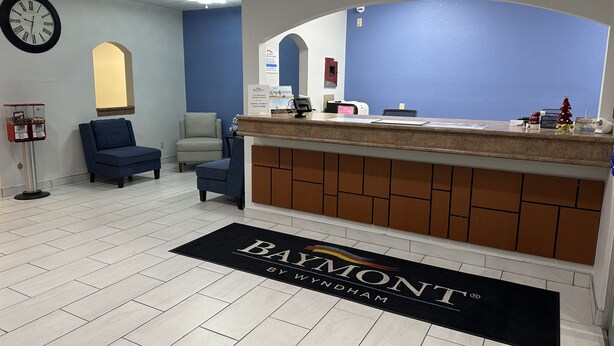 A reception area with a blue wall, a reception desk, a clock, and a chair. - Baymont by Wyndham Omaha SW (Omaha)