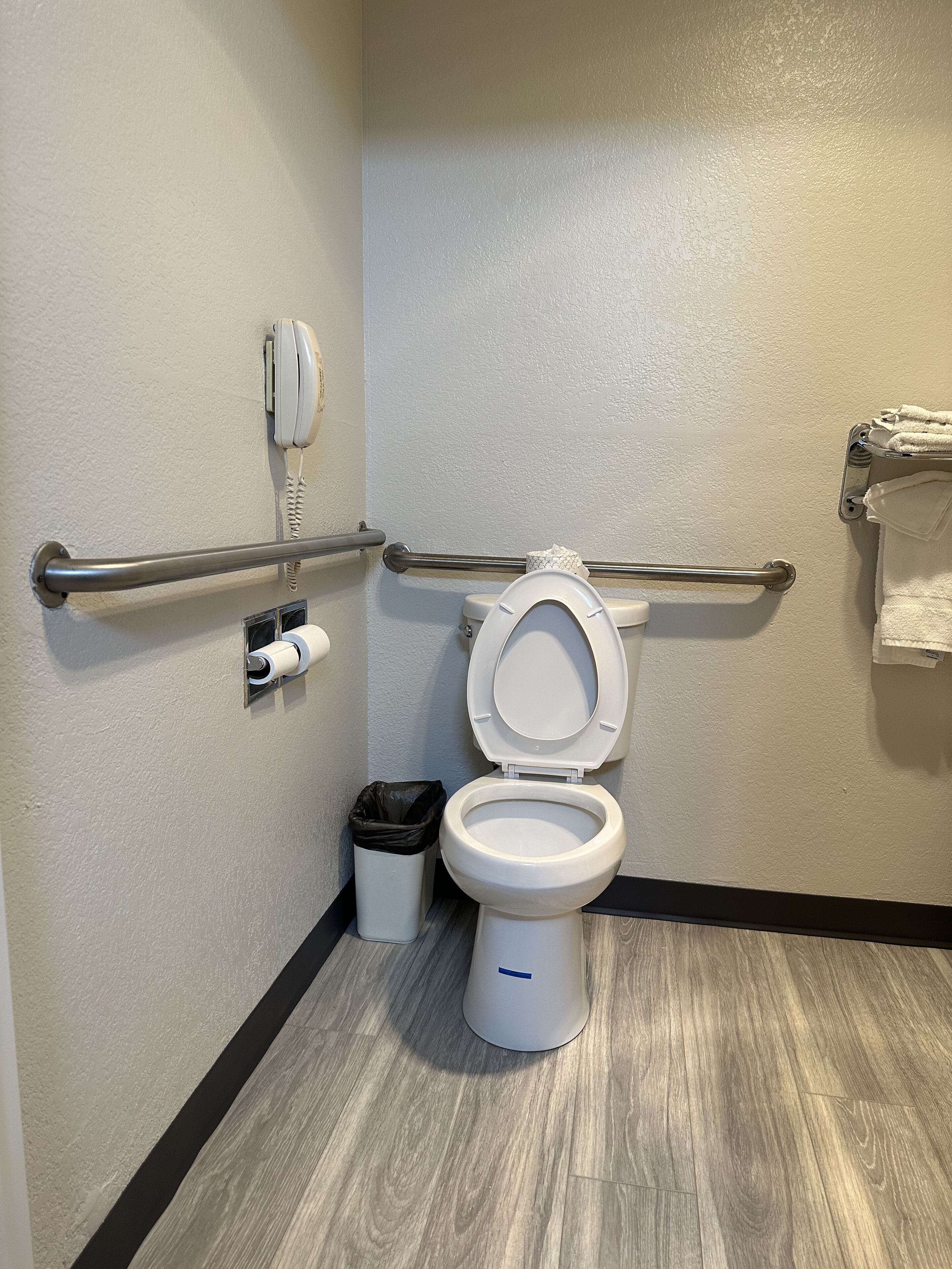 A bathroom with a white toilet, a hand dryer, a trash can, and a towel rack.