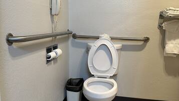 A bathroom with a white toilet, a hand dryer, a trash can, and a towel rack.