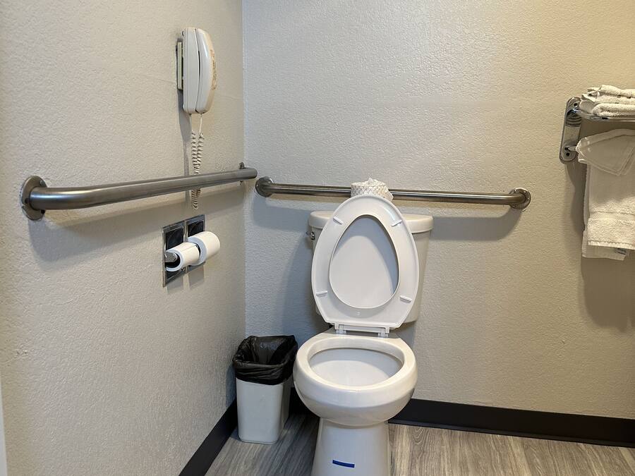 A bathroom with a white toilet, a hand dryer, a trash can, and a towel rack.