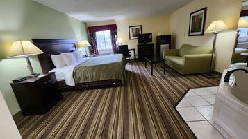 Quarto de hotel com cama, escrivaninha, cadeira, televisão, mesinha e banheiro.