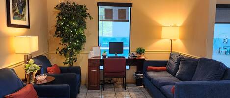 Een gezellige kamer met twee banken, een bureau met een computer, een grote plant en een raam met uitzicht.