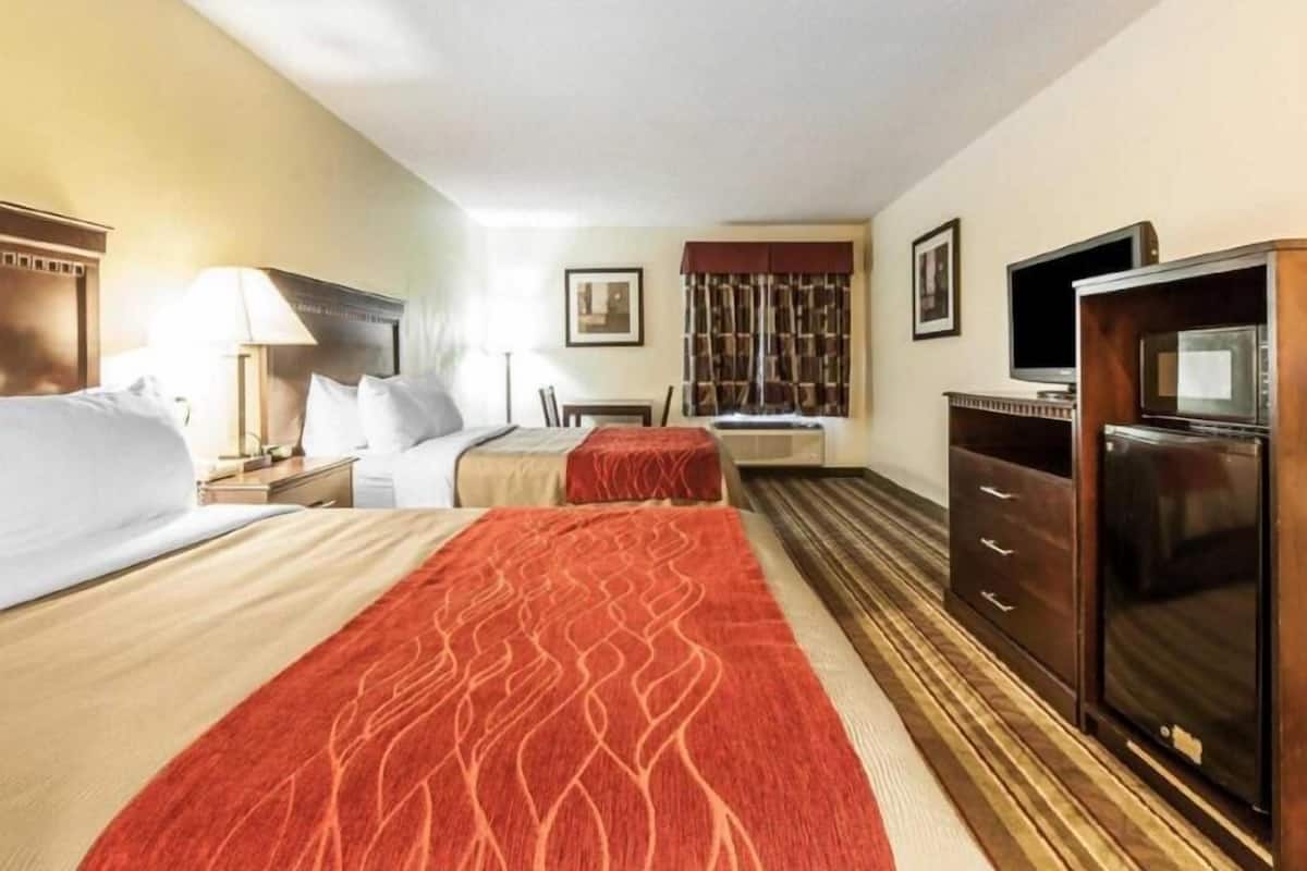 A hotel room with two beds, a TV, a minibar, and a window with curtains.
