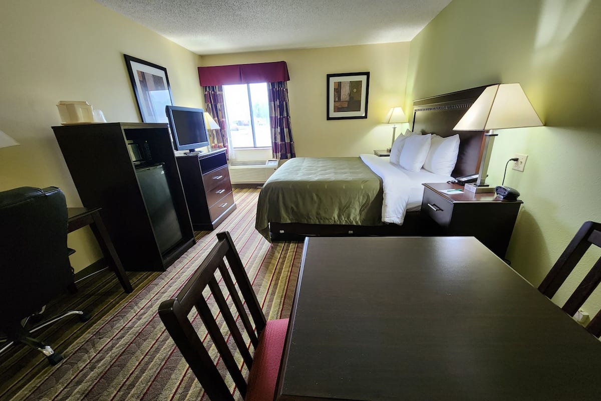 A hotel room with a bed, desk, chair, TV, refrigerator, and a window with curtains.