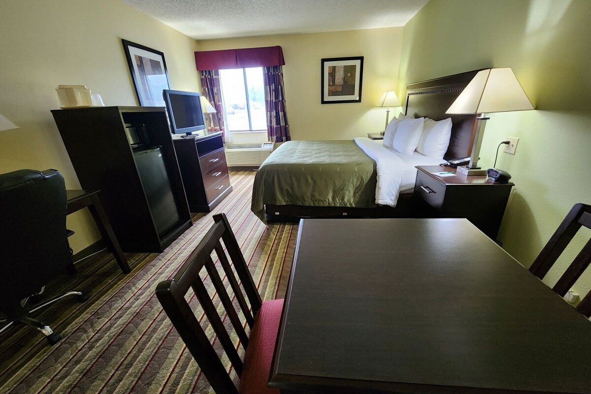 A hotel room with a bed, desk, chair, television, and a small kitchenette.