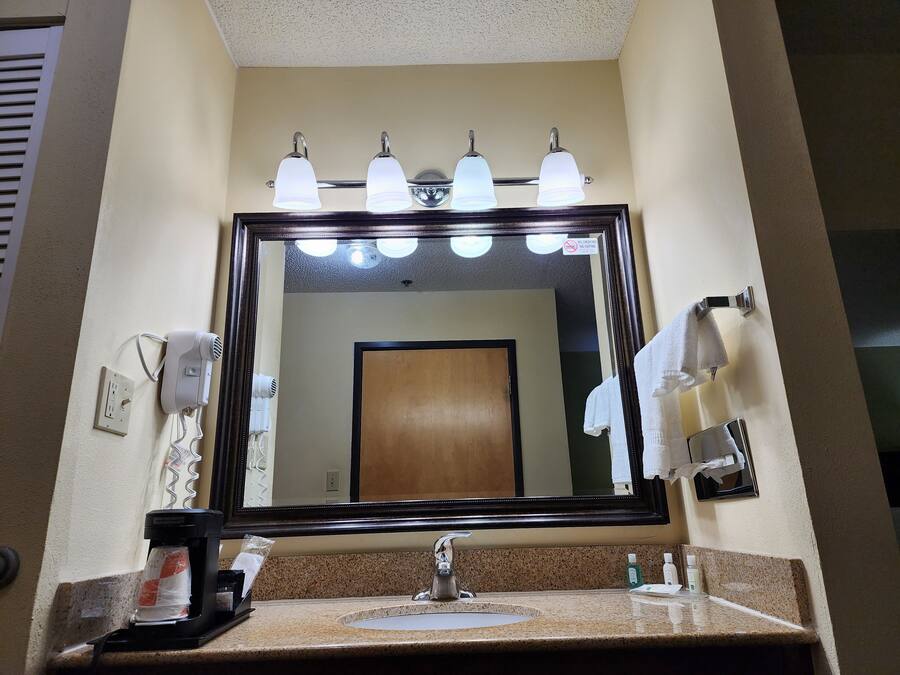 A hotel bathroom with a large mirror, a sink, a hairdryer, and a coffee maker.