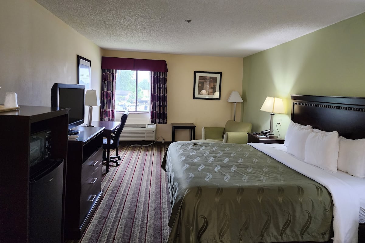 A hotel room with a bed, desk, chair, television, and a window with curtains.