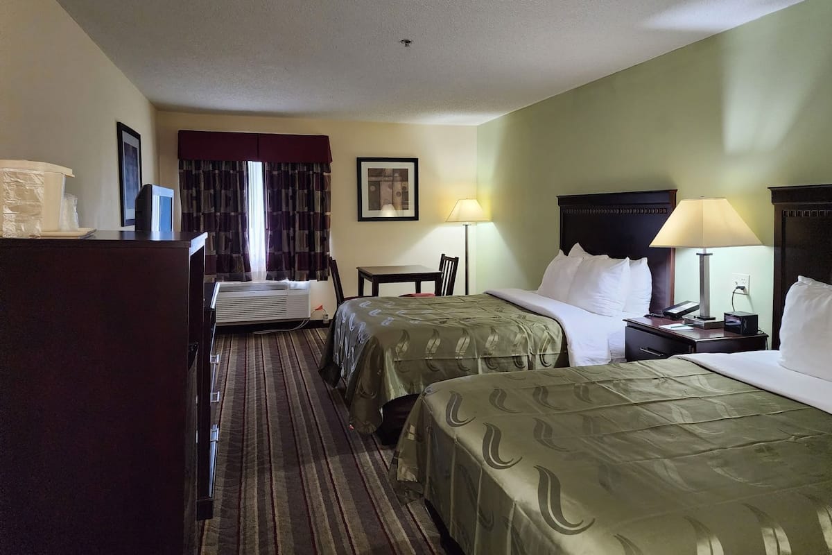 A hotel room with two beds, a desk, a chair, a lamp, and a picture on the wall.