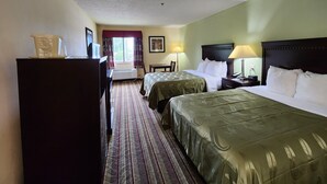 Ein Hotelzimmer mit zwei Betten, einem Schreibtisch, einem Stuhl, einer Kommode und einem Fenster mit Vorhängen.