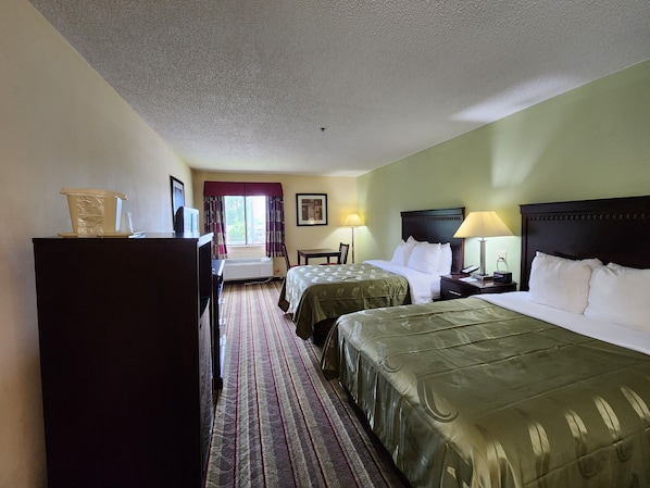 A hotel room with two beds, a desk, a chair, a dresser, and a window with curtains.