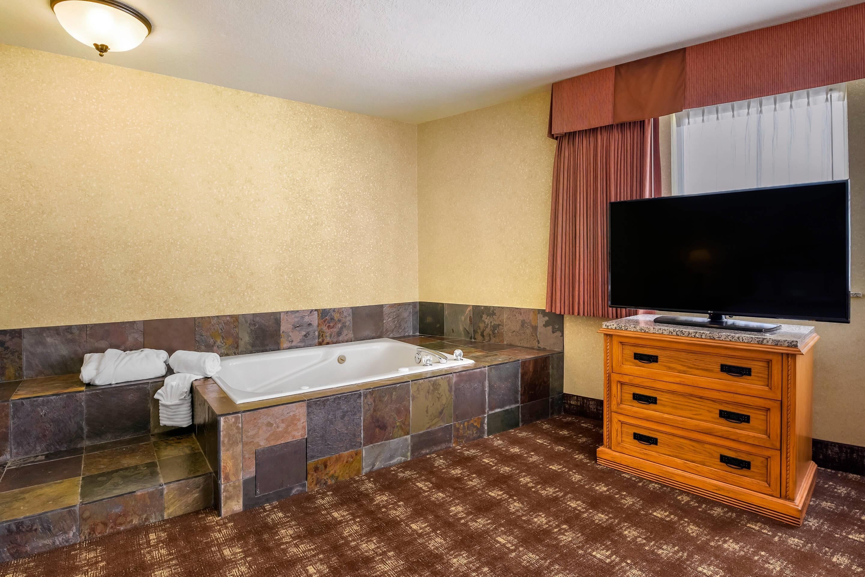 A bathroom with a bathtub, a vanity with drawers, and a television.