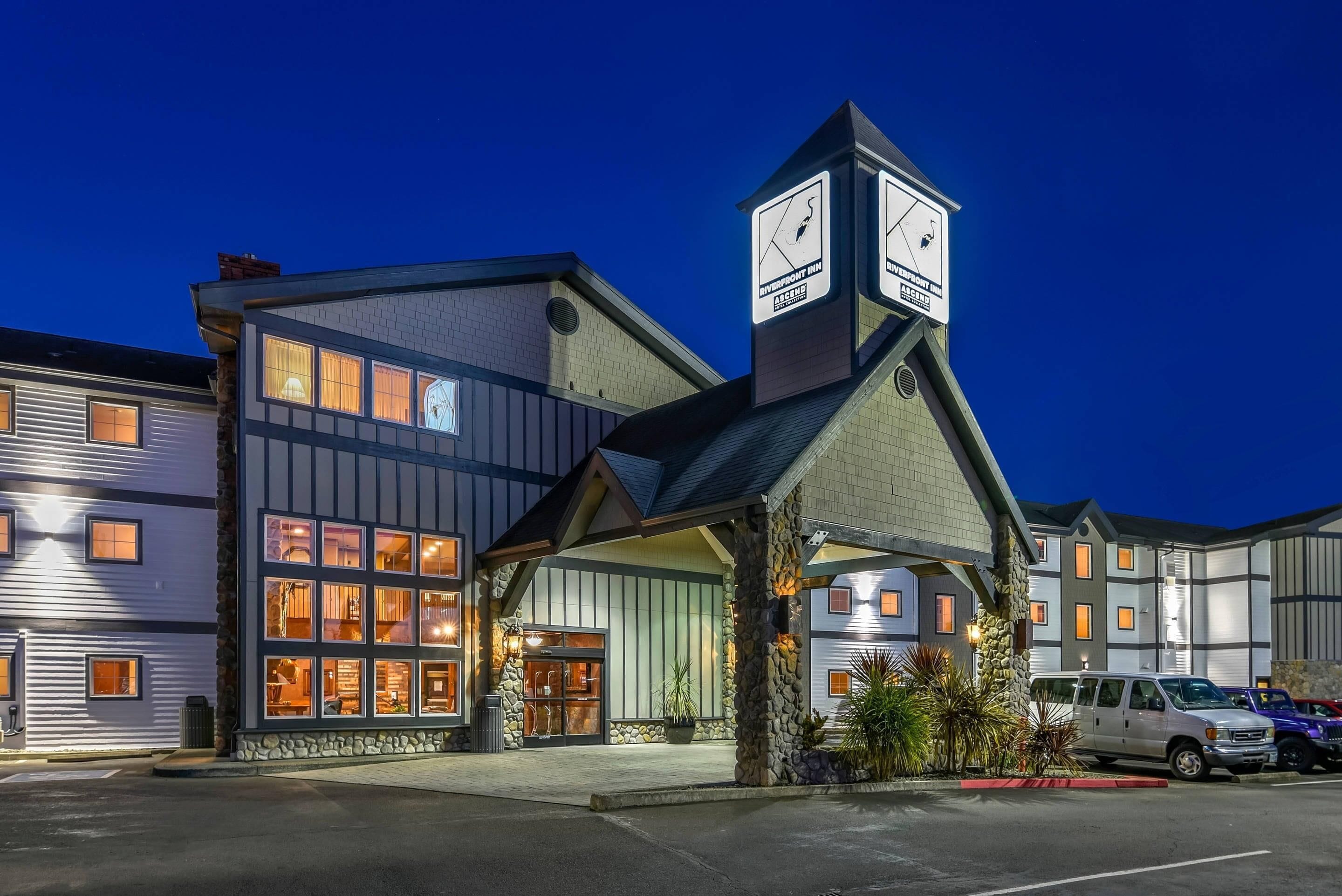 A hotel with a clock tower, a stone facade, and a parking lot.