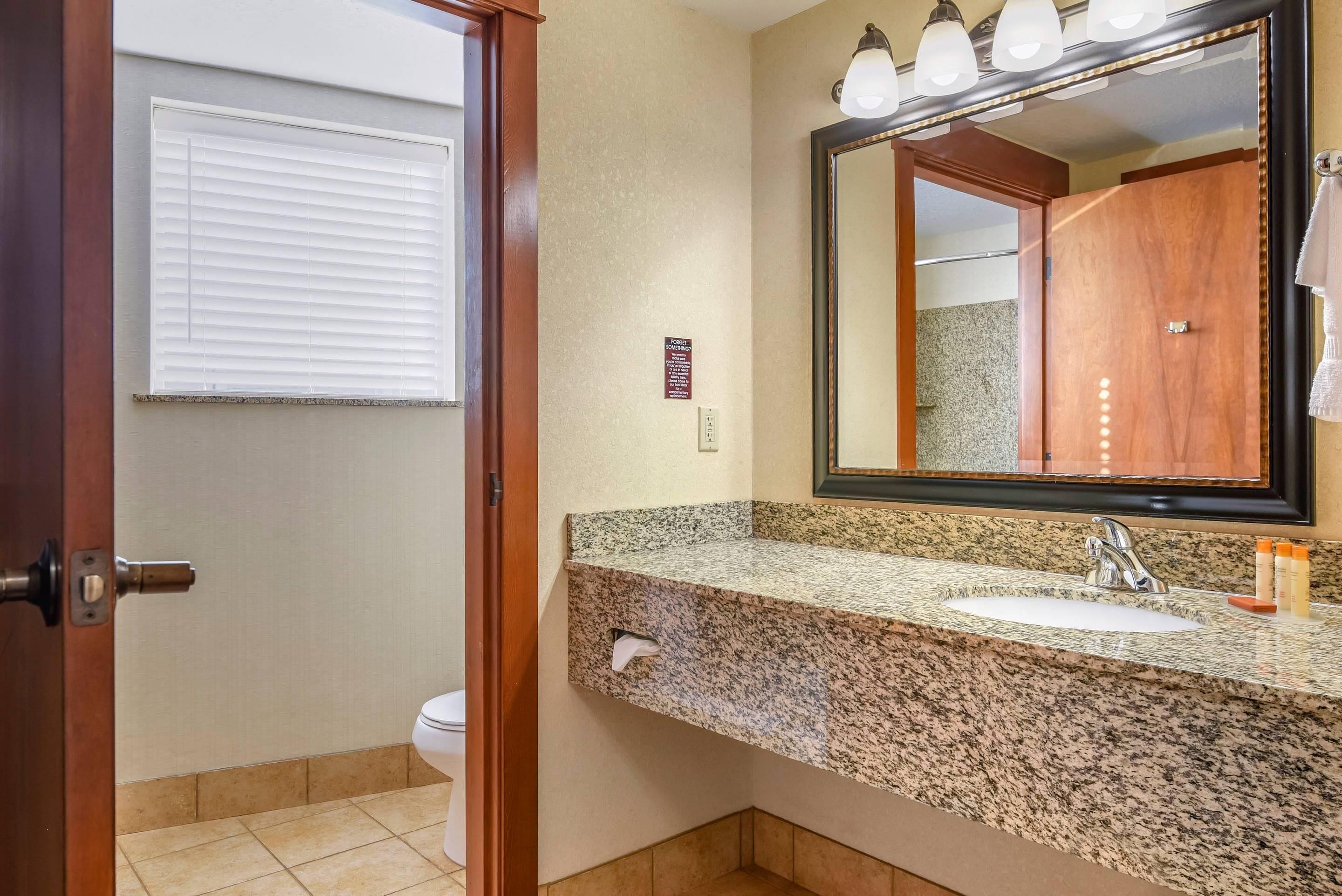 A bathroom with a granite countertop, a sink, a mirror, and a toilet.