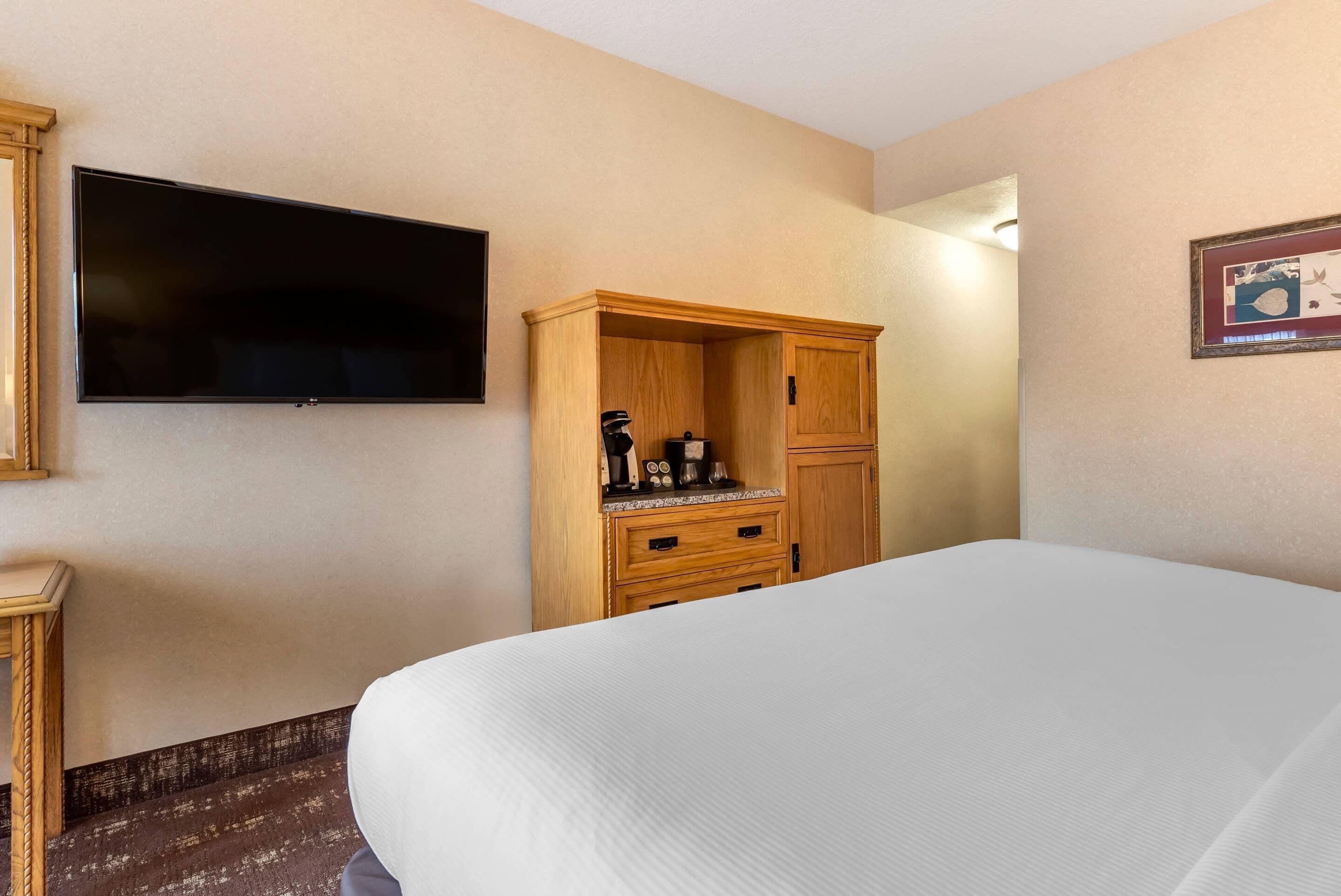 Une chambre d’hôtel dotée d’un grand lit, d’un téléviseur à écran plat fixé au mur, d’une armoire en bois et d’une petite table avec une machine à café.