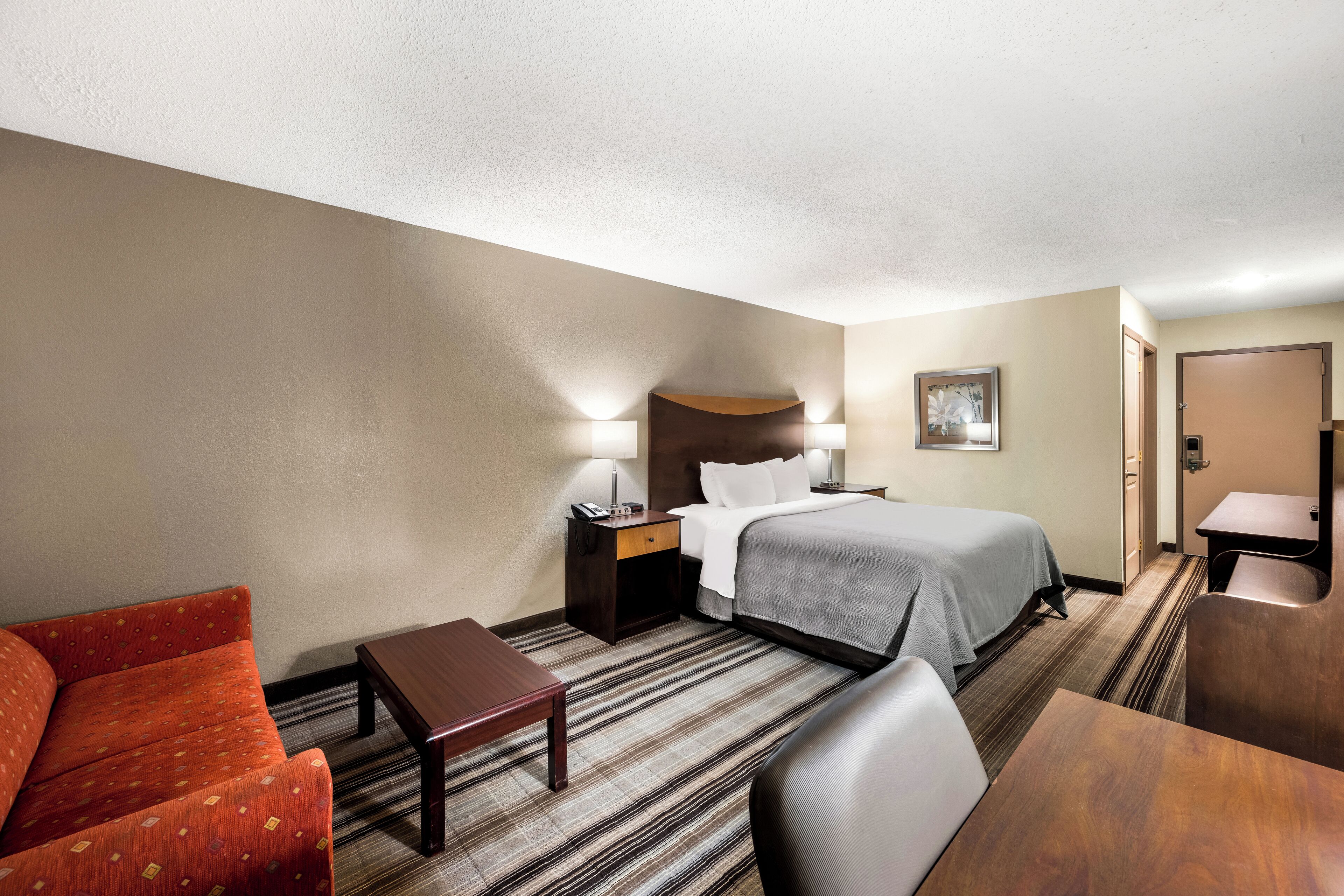 Ein Hotelzimmer mit Bett, Schreibtisch, Stuhl, Sofa und Nachttisch mit Lampe.