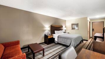 Ein Hotelzimmer mit Bett, Schreibtisch, Stuhl, Sofa und Nachttisch mit Lampe.
