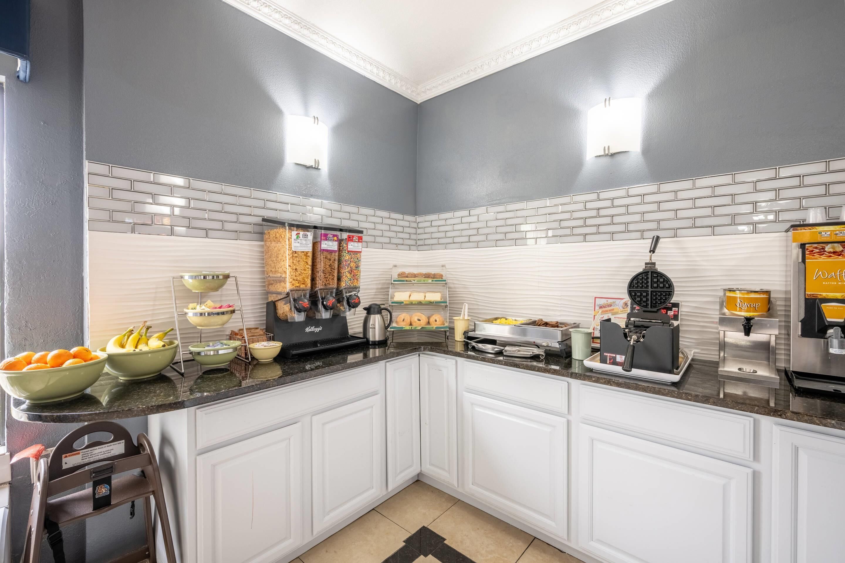 Una cucina moderna con mobili bianchi, uno schienale in mattoni e diversi elettrodomestici, tra cui una piastra per waffle e una macchina per caffè.