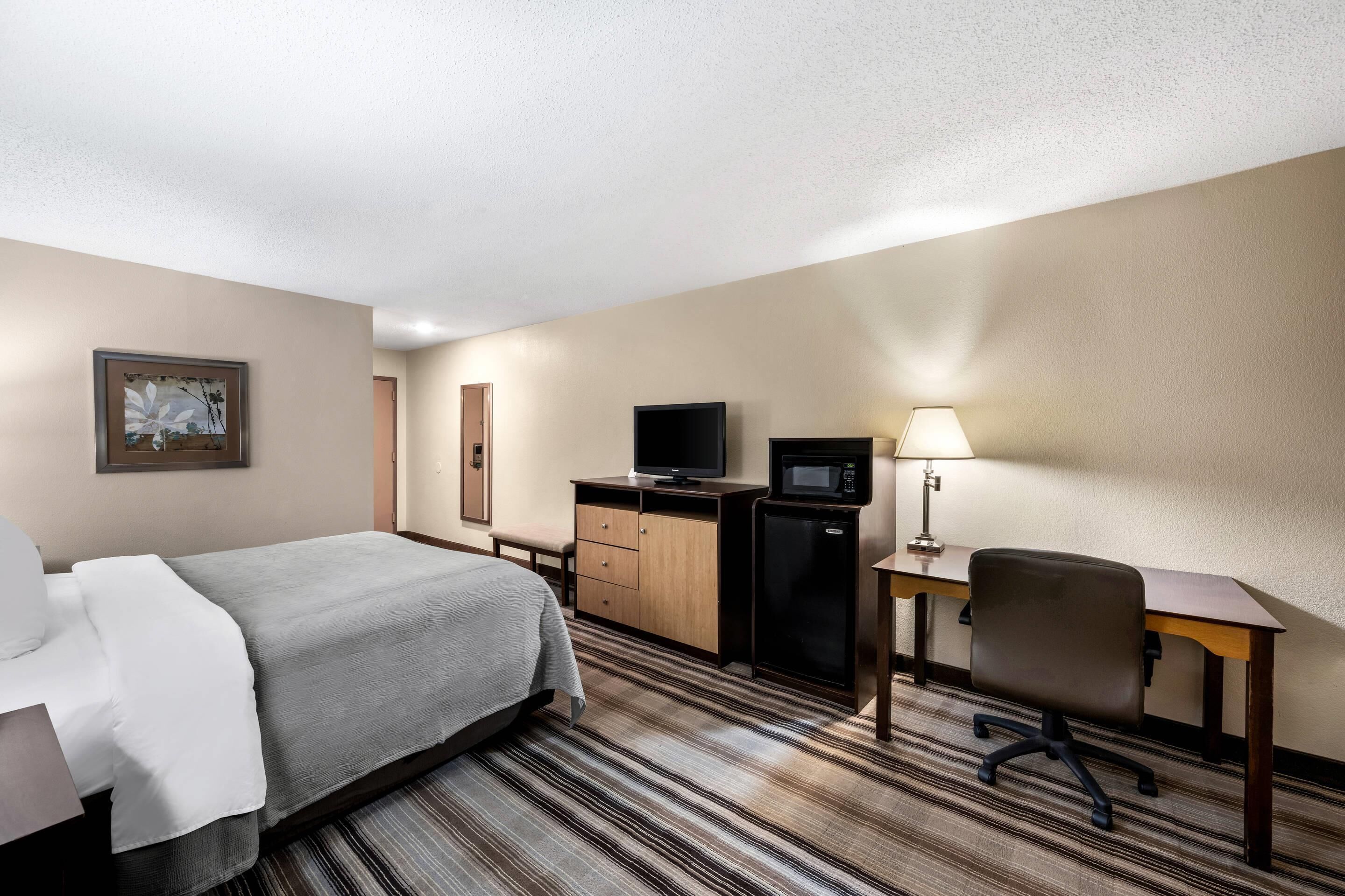 Ein Hotelzimmer mit Bett, Schreibtisch, Fernseher, Mikrowelle und Lampe.