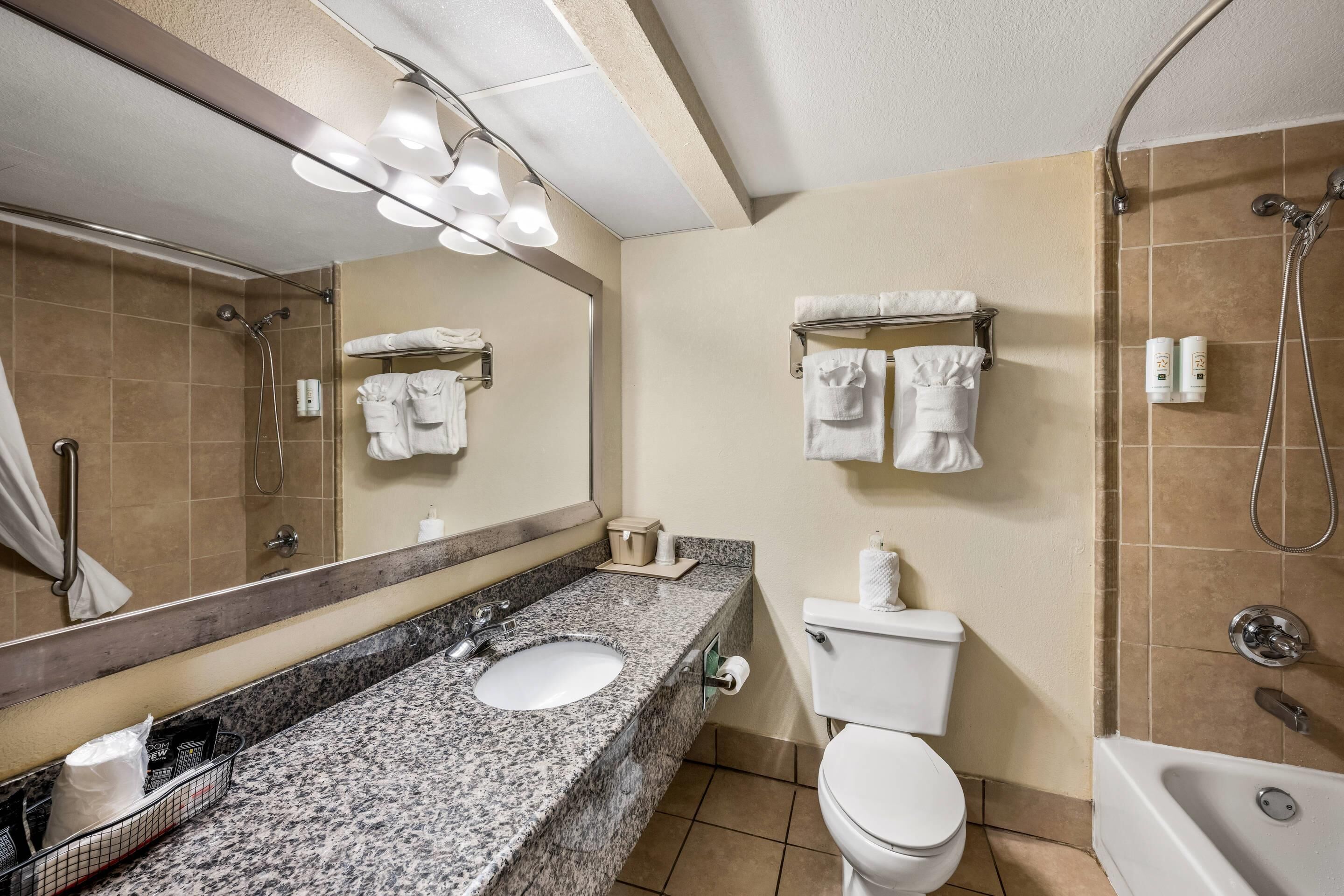 A bathroom with a granite sink, white toilet, and a bathtub.