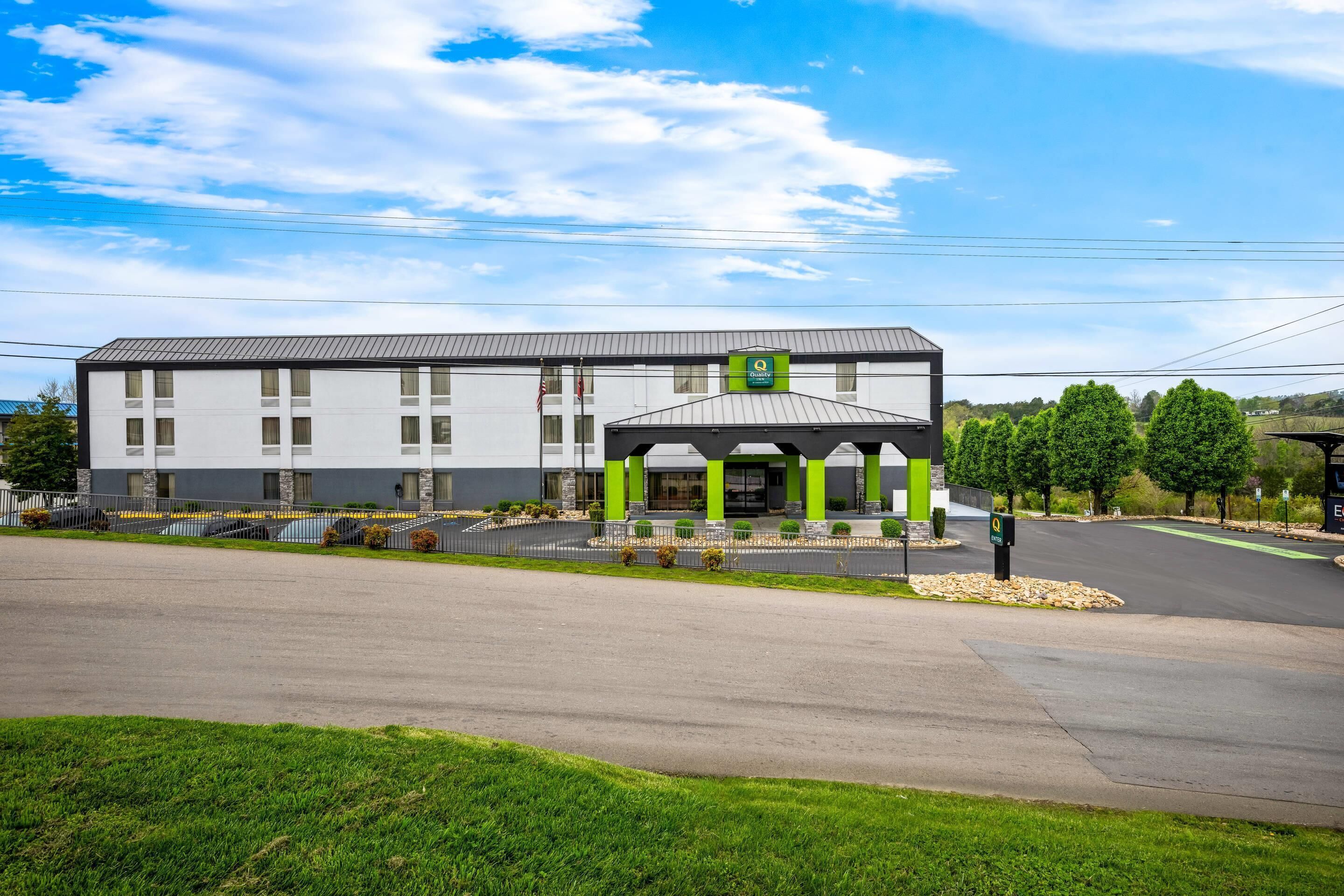 A modern hotel with a covered entrance, a parking lot, and a well-maintained lawn.