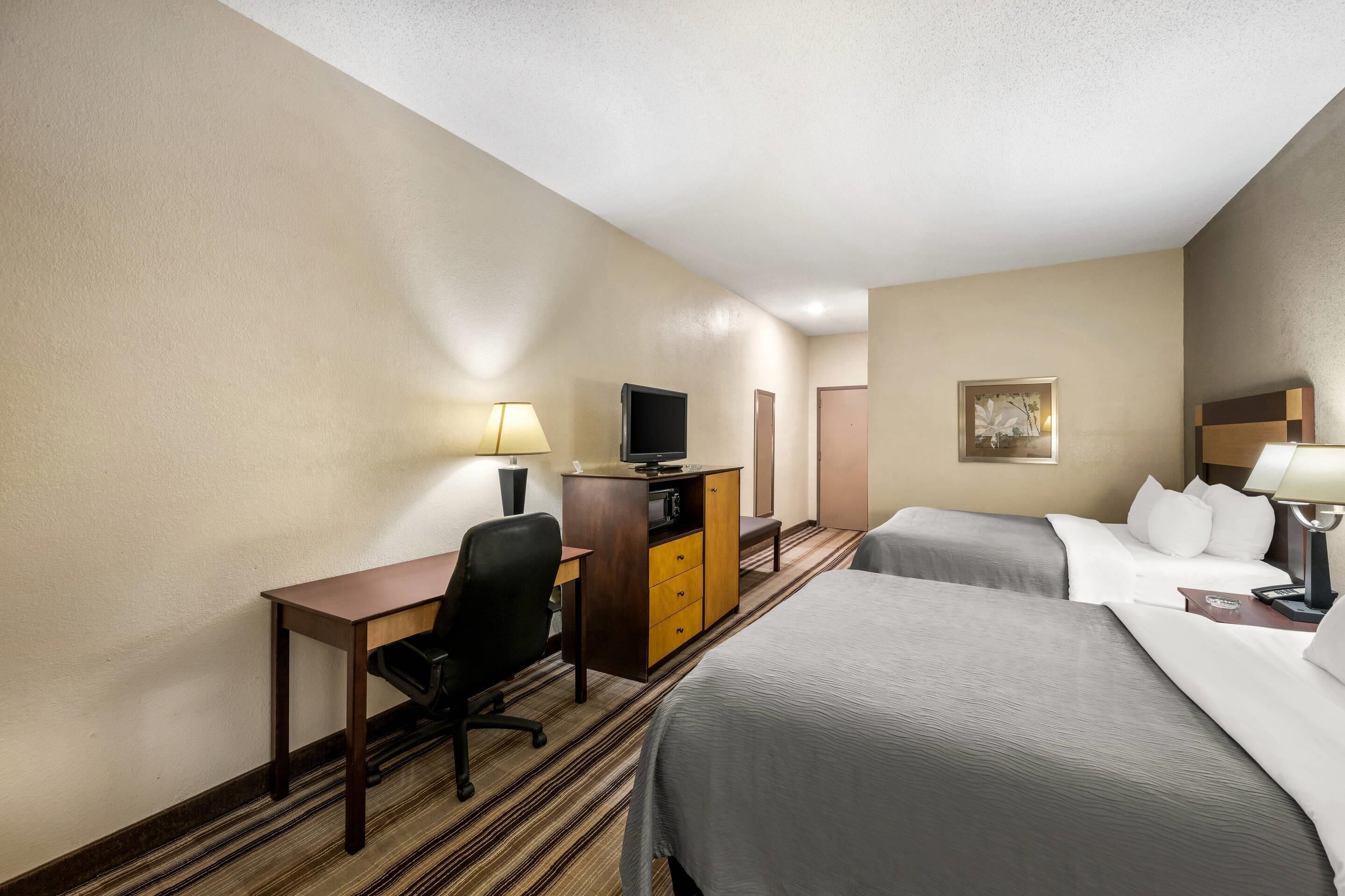 A hotel room with two beds, a desk with a chair, a television, a dresser, and a lamp.