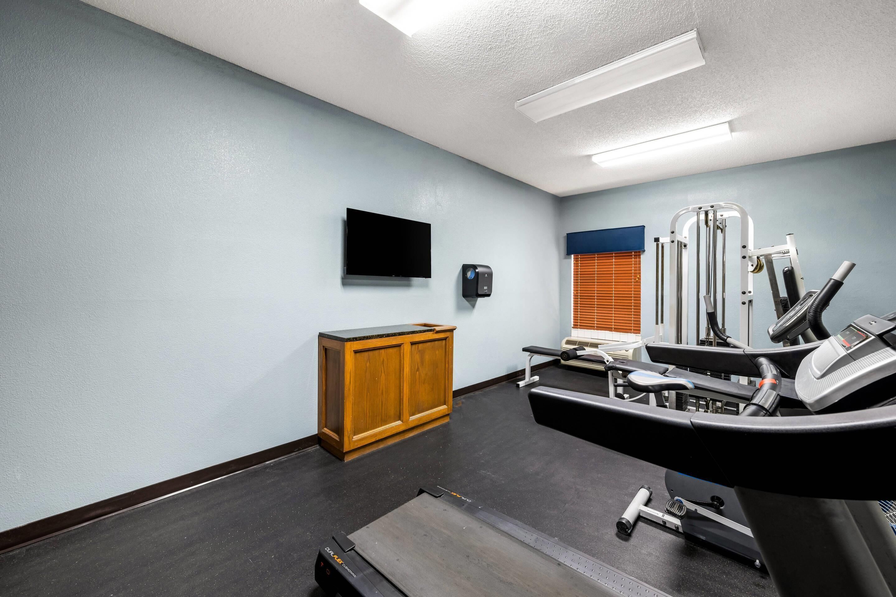 A gym with exercise equipment, a television, and a wooden cabinet.