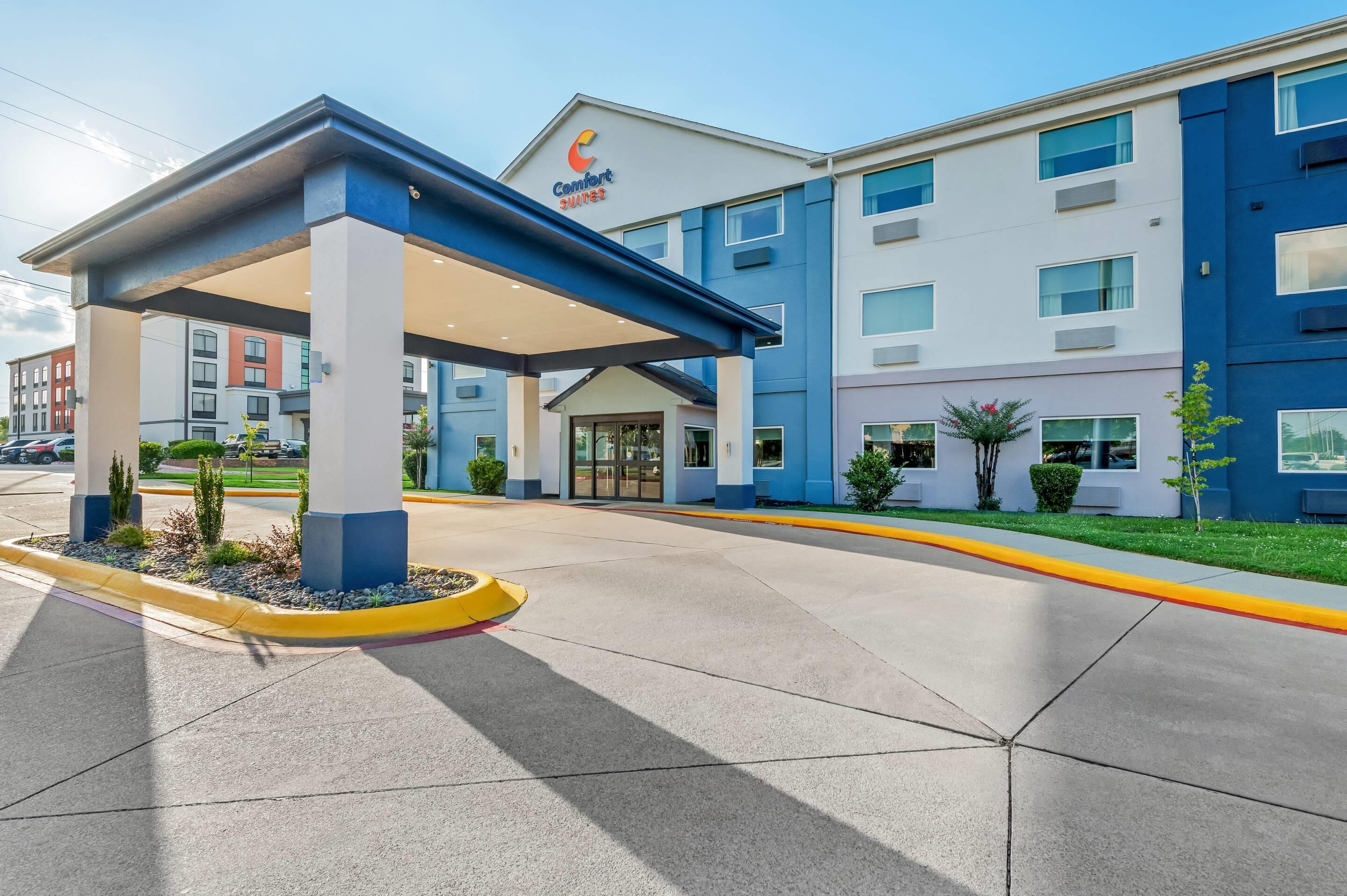 A hotel entrance with a covered outdoor area, a clear sky, and a parking lot.