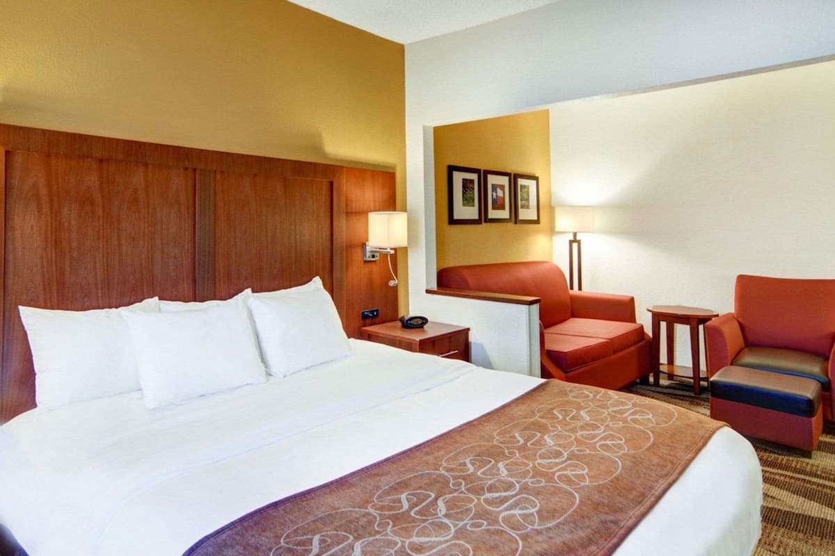 A hotel room with a large bed, a wooden headboard, a desk, a chair, and a small table.