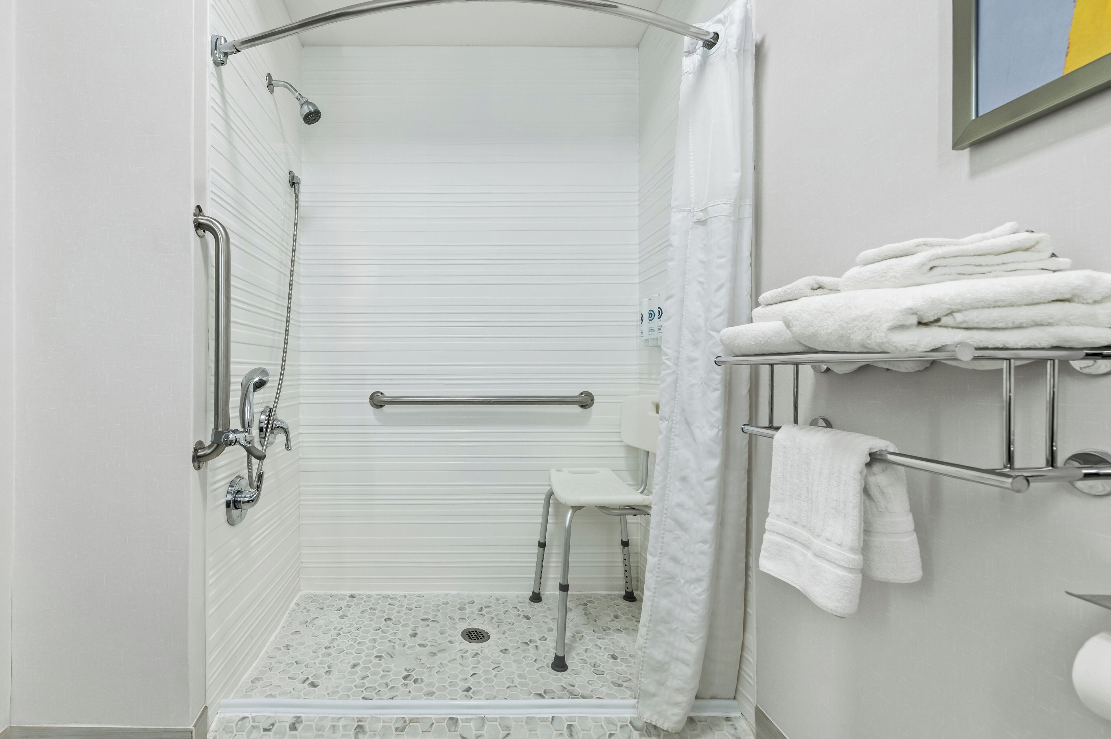 A bathroom with a shower, grab bars, a white toilet, and a towel rack.