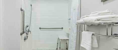 A bathroom with a shower, grab bars, a white toilet, and a towel rack.